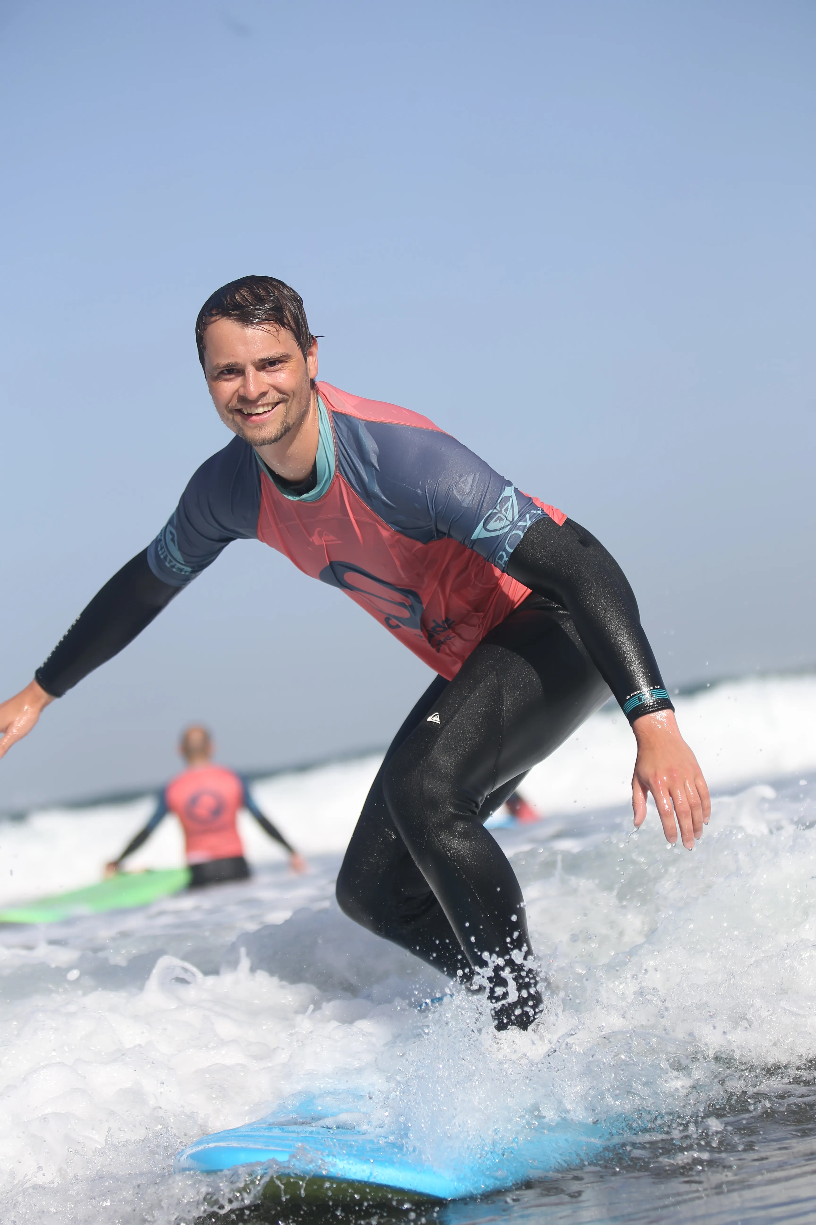 Connor stands crouched on a surfboard riding a small wave in front of a cloudy sky