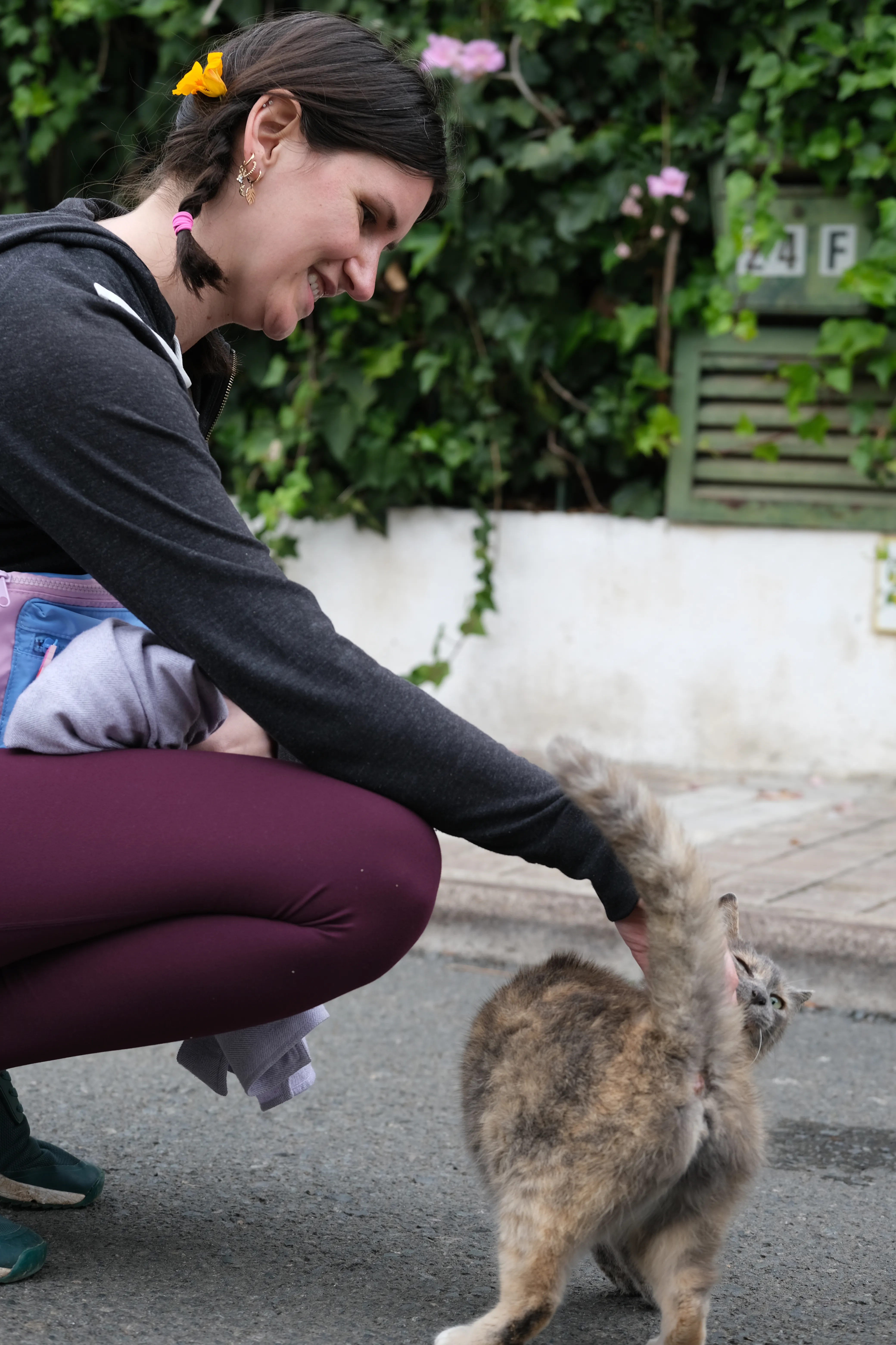 Jillian pets a grey-brown cat on a street. A yellow flower adorns her hair.