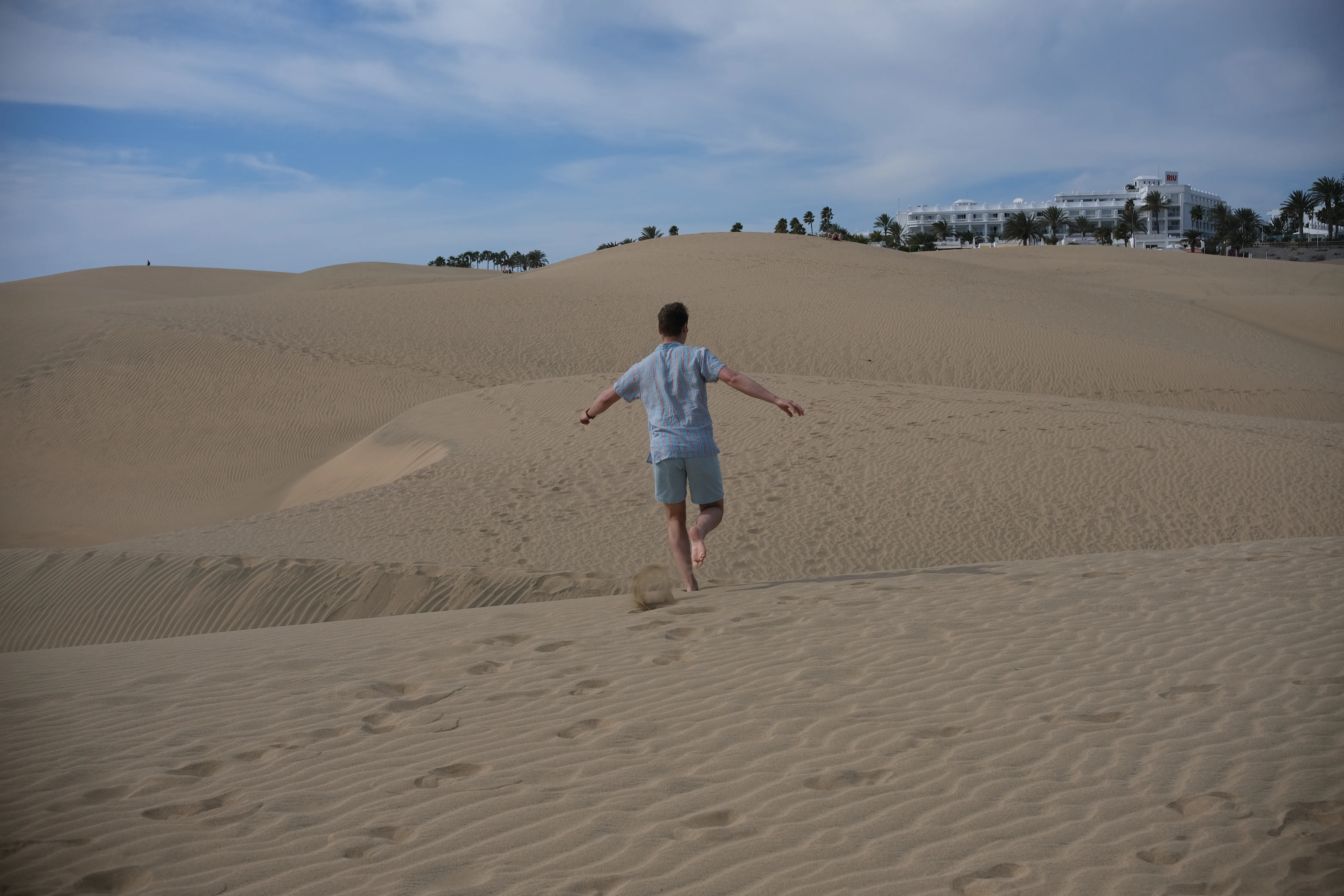 Connor takes a running leap of the ridge of a sand dune, spreading his arms for balance.