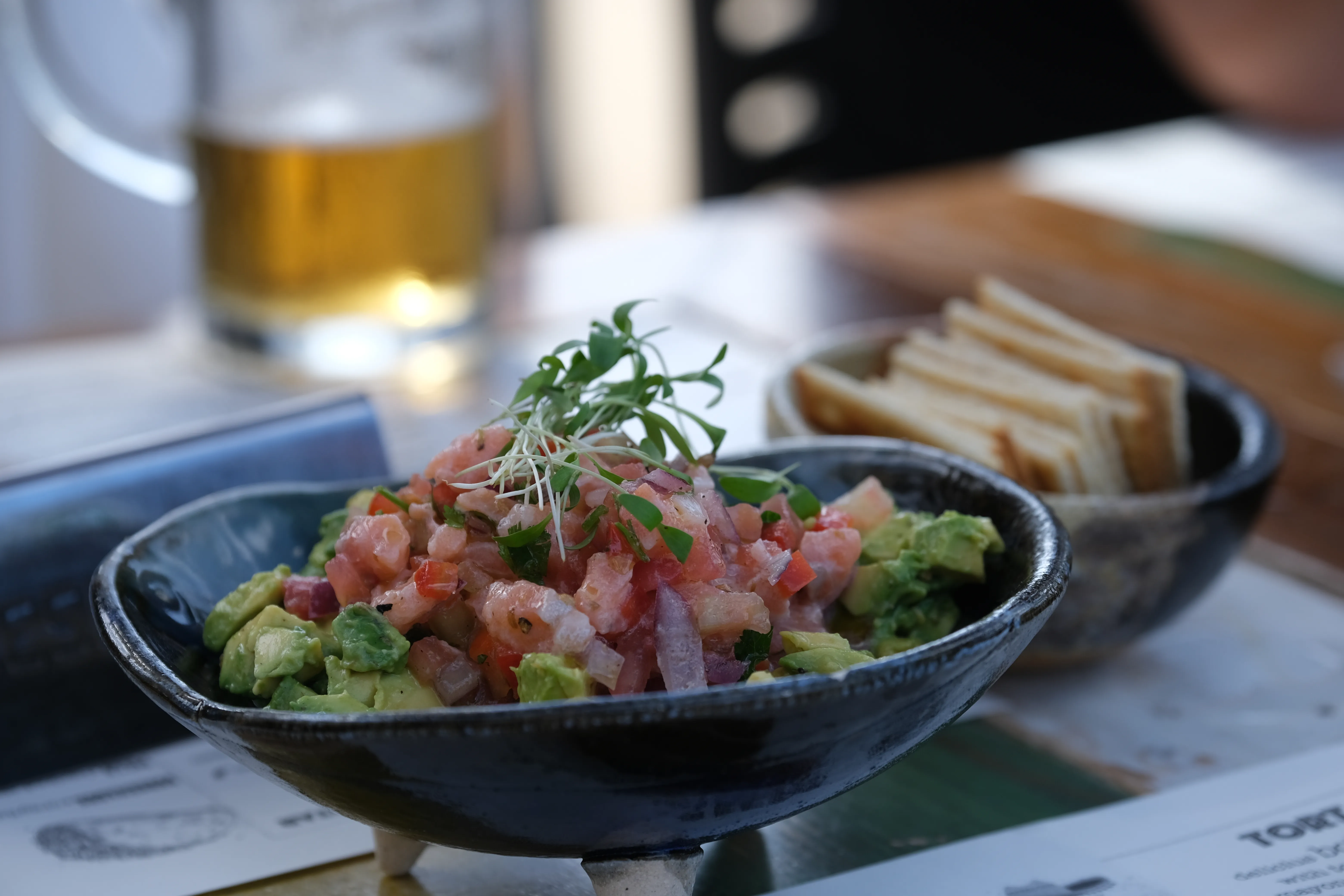 A handmade bowl of salmon ceviche with avocado, flanked by a small bowl of crackers.